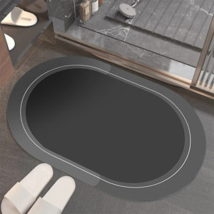 Ce tapis est ovale . Il est placé devant une douche avec des chaussons. Il est noir.