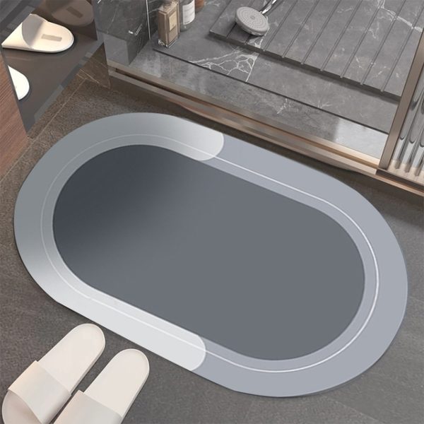 Ce tapis est ovale . Il est placé devant une douche avec des chaussons. Il est gris.