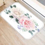 Ce tapis à fleur est rectangulaire. Il est blanc et les fleurs sont des roses. Il est placé sur un parquet.