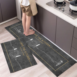 2 tapis gris avec motifs de couverts et "love the kitchen". Parquet marron clair et meuble de cuisine gris. On voit les jambes d'une personne cuisinant.