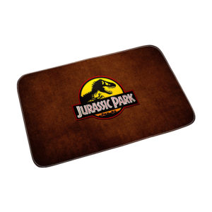 Paillasson rectangulaire Jurassic Park. Il est marron et possède le logo de la saga en jaune. Fond blanc.