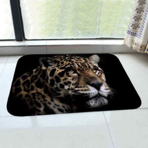 Paillasson noir avec une tete de leopard pose sur du carrelage devant une baie vitree