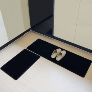 2 paillassons noirs posés dans une cuisine sur un sol blanc. On voit du mobilier de cuisine et des chaussons posés sur le grand paillasson.