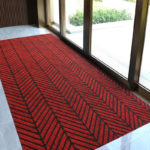 Paillasson rouge à chevrons posé devant une grande porte baie-vitree