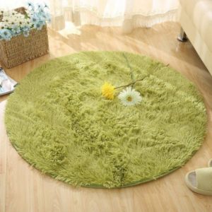 Ce tapis rond est vert . Il est disposé sur du parquet. Un casier en osier avec des fleurs est placé sur le coin supérieur gauche.