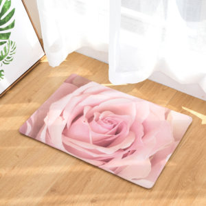Paillasson imprime d'une rose rose pose sur du parquet devat une porte fenetre avec un rideau blanc