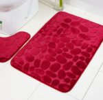 Ce paillasson est rouge avec des motifs pavés. Il est placé dans une salle de bain.
