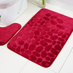 Ce paillasson est rouge avec des motifs pavés. Il est placé dans une salle de bain.