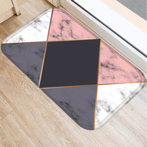 Tapis rectangulaire avec lignes en triangles, couleurs rose, noir gris et blanc. En fond, parquet marron clair et bordure de fenêtre.
