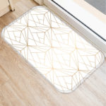 Paillasson blanc avec lignes or rosé. Parquet marron clair et bordure de fenêtre.