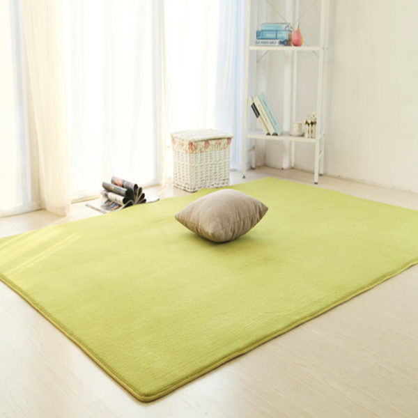 Ce tapis est vert et rectangulaire. Il est placé sous une fenêtre dans une chambre. Un coussin est posé dessus.
